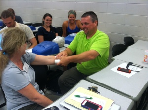 Field Assistant Joey wraps a (pretend) gash on Dr. Peres's forearm. The students are amused.